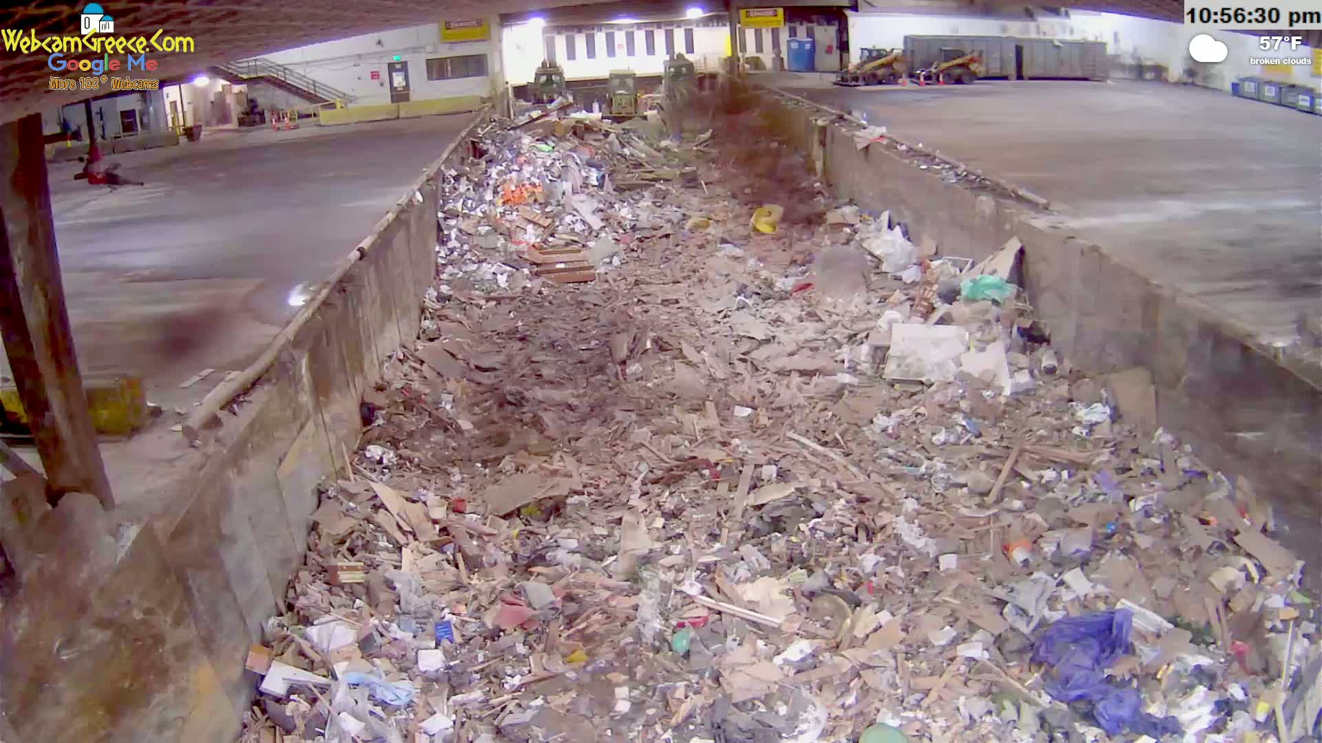 A large pile of refuse fills a long, concrete trough under broken clouds at 57°F.