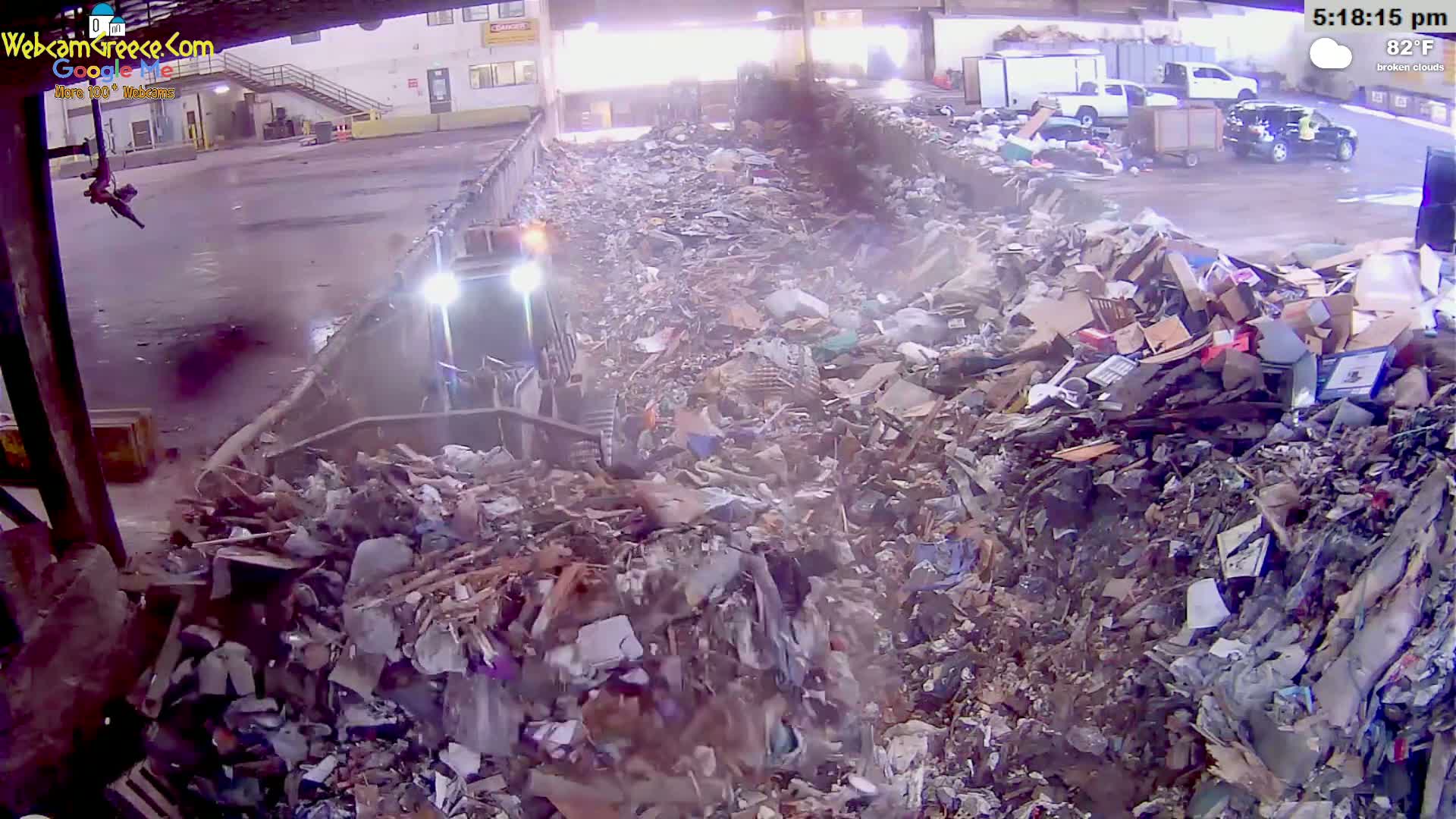A large pile of mixed waste is being compacted by a machine under partly cloudy skies.