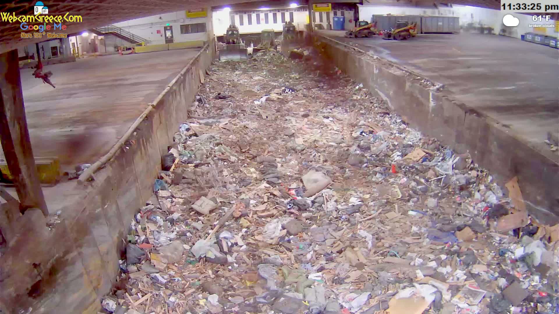 A large pile of trash and debris fills a long, narrow concrete trough inside a building under broken clouds and a 61°F temperature.