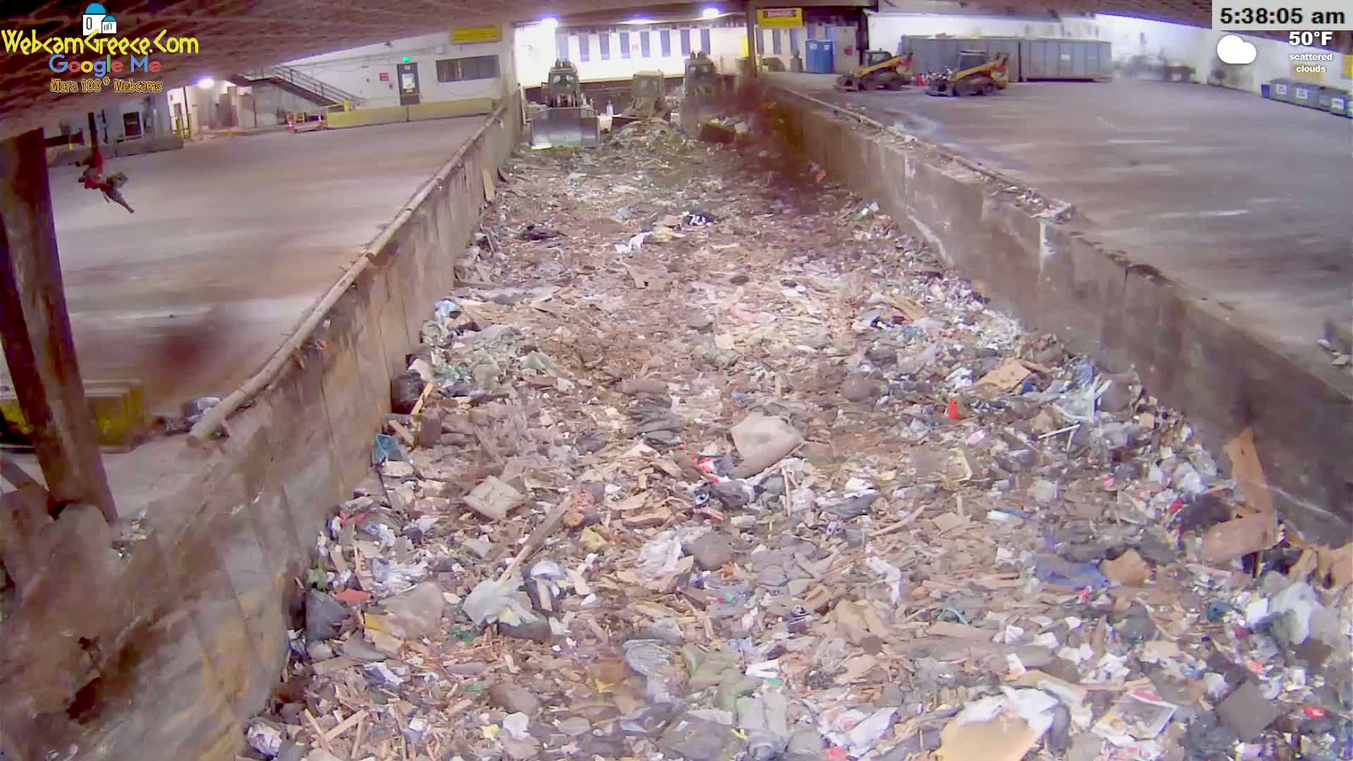 A large pile of trash fills a concrete trough in an indoor facility under scattered clouds and 50°F weather.