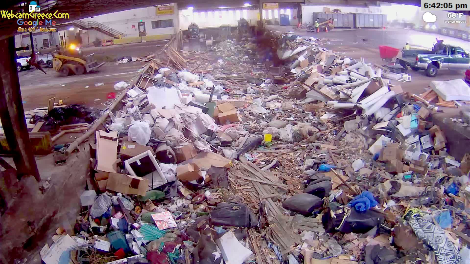 A large pile of discarded materials, including furniture, boxes, and other debris, sits under a partly cloudy sky with a temperature of 68°F.