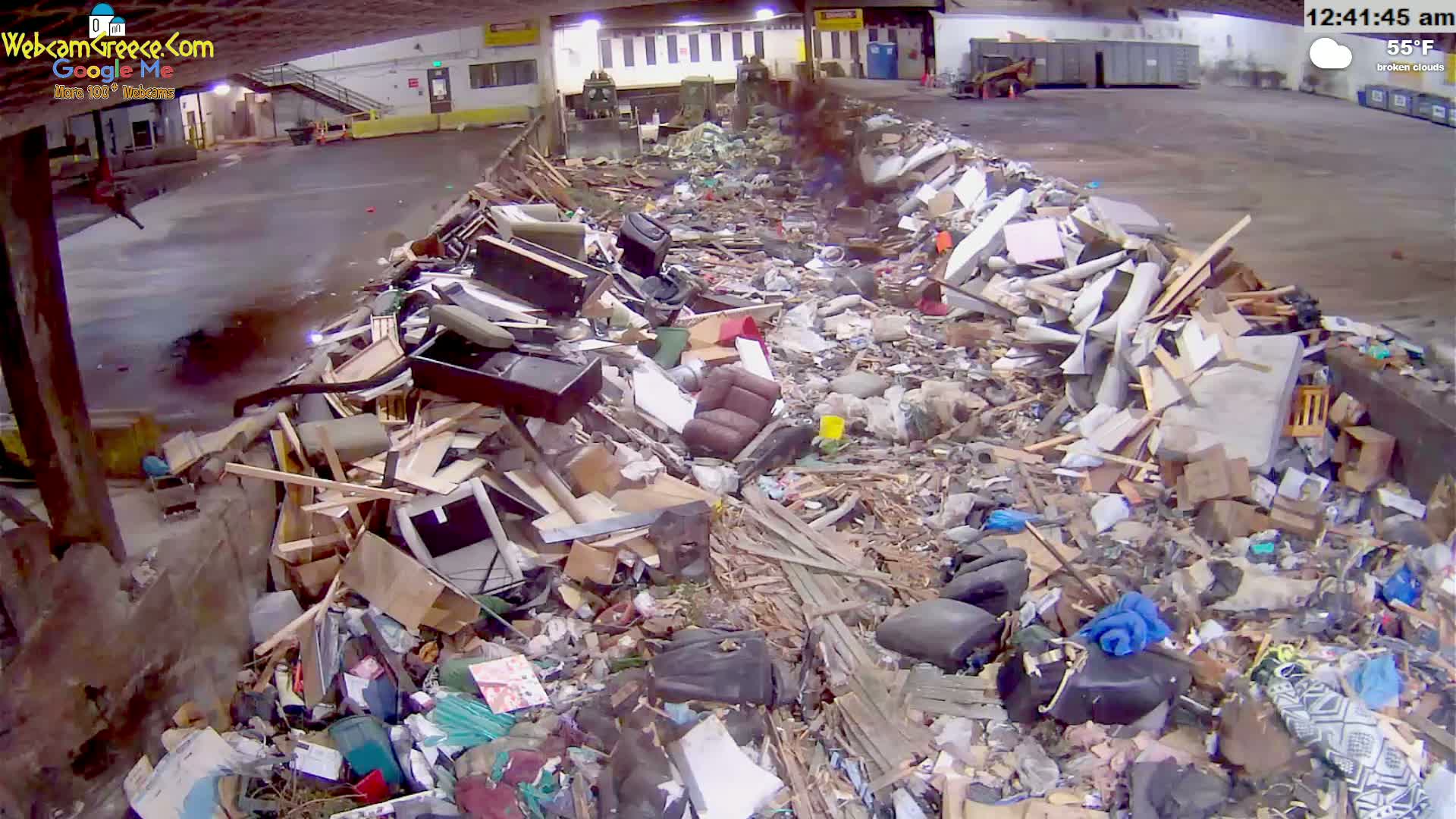 A large pile of discarded furniture and debris sits inside a building under broken clouds with a temperature of 55°F.