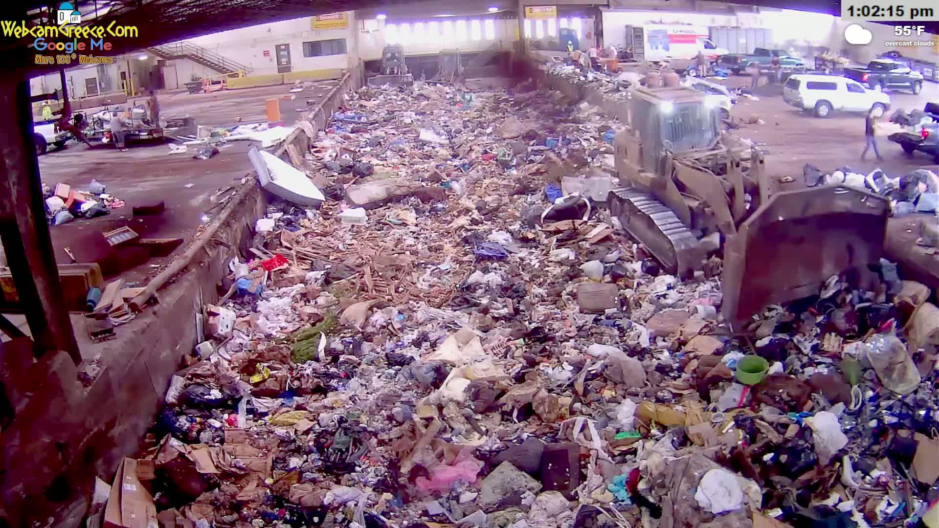 A large pile of trash is being compacted by a bulldozer under overcast skies.