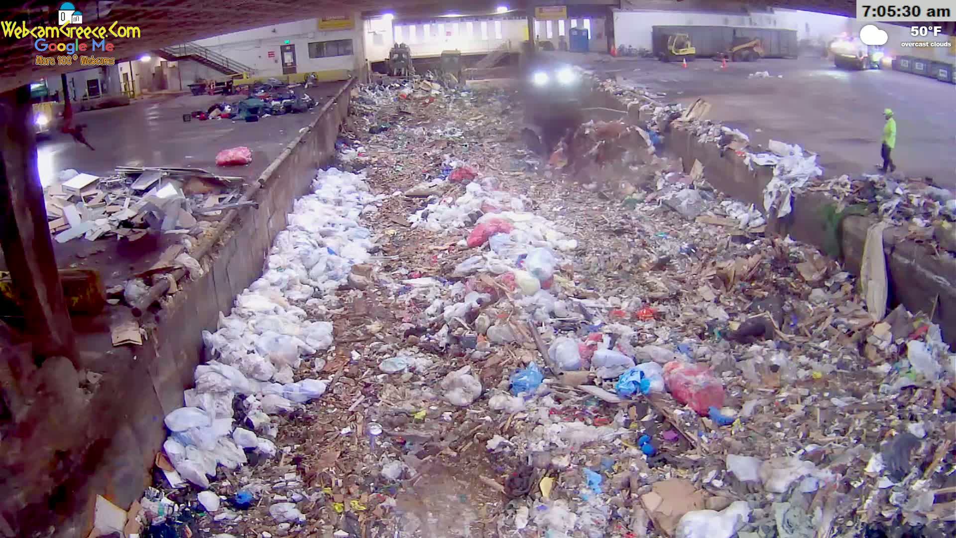 A large pile of trash and debris sits in an outdoor area under overcast skies, with a person visible in the distance.