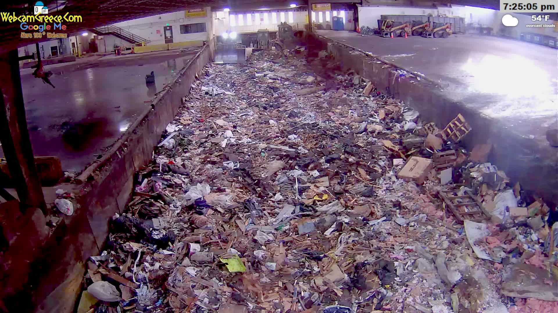 A large pile of refuse is contained within a long, trough-like structure under overcast skies.