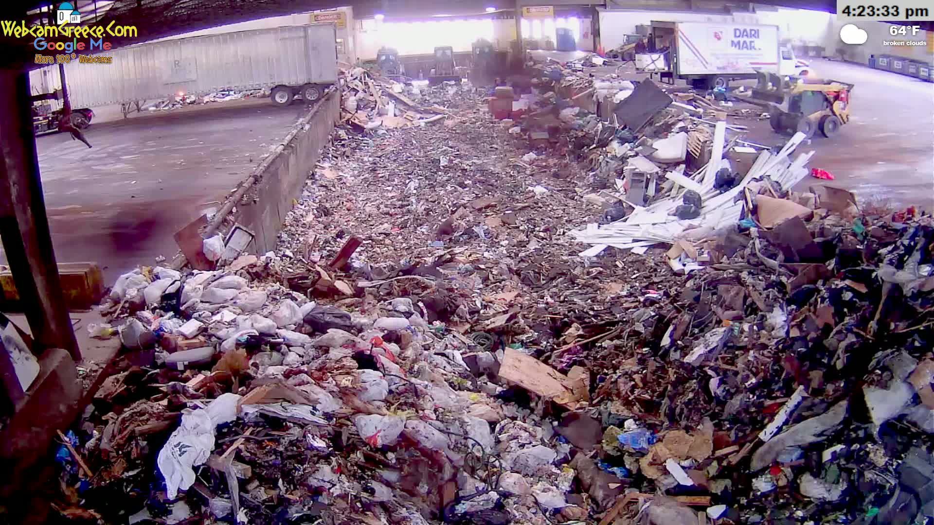 A large pile of trash and debris sits between two trucks under a covered area on a partly cloudy day.