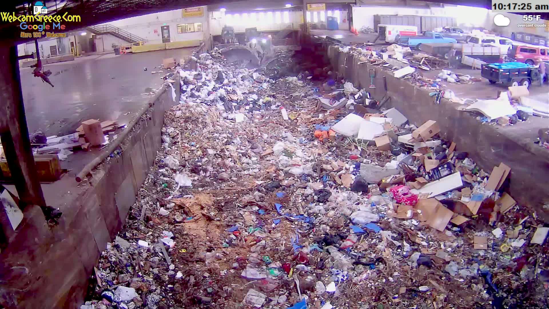 A large pile of trash and debris fills a concrete trough under overcast skies, with machinery visible in the background.