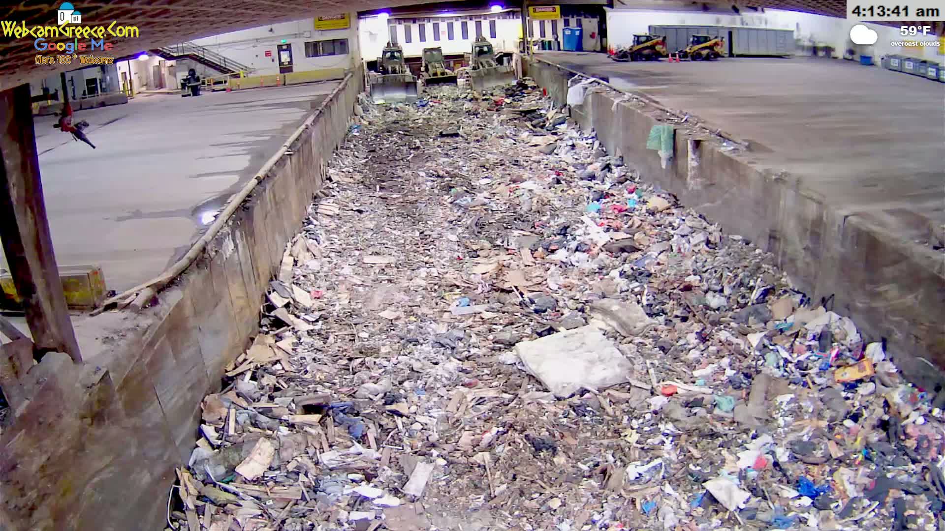 A large pile of garbage fills a long, narrow trough inside a building under overcast skies at 59°F.