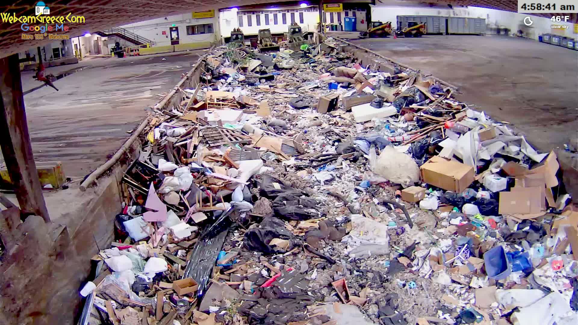 A large pile of mixed garbage and debris fills a long, low trough-like structure in an indoor facility under clear skies.