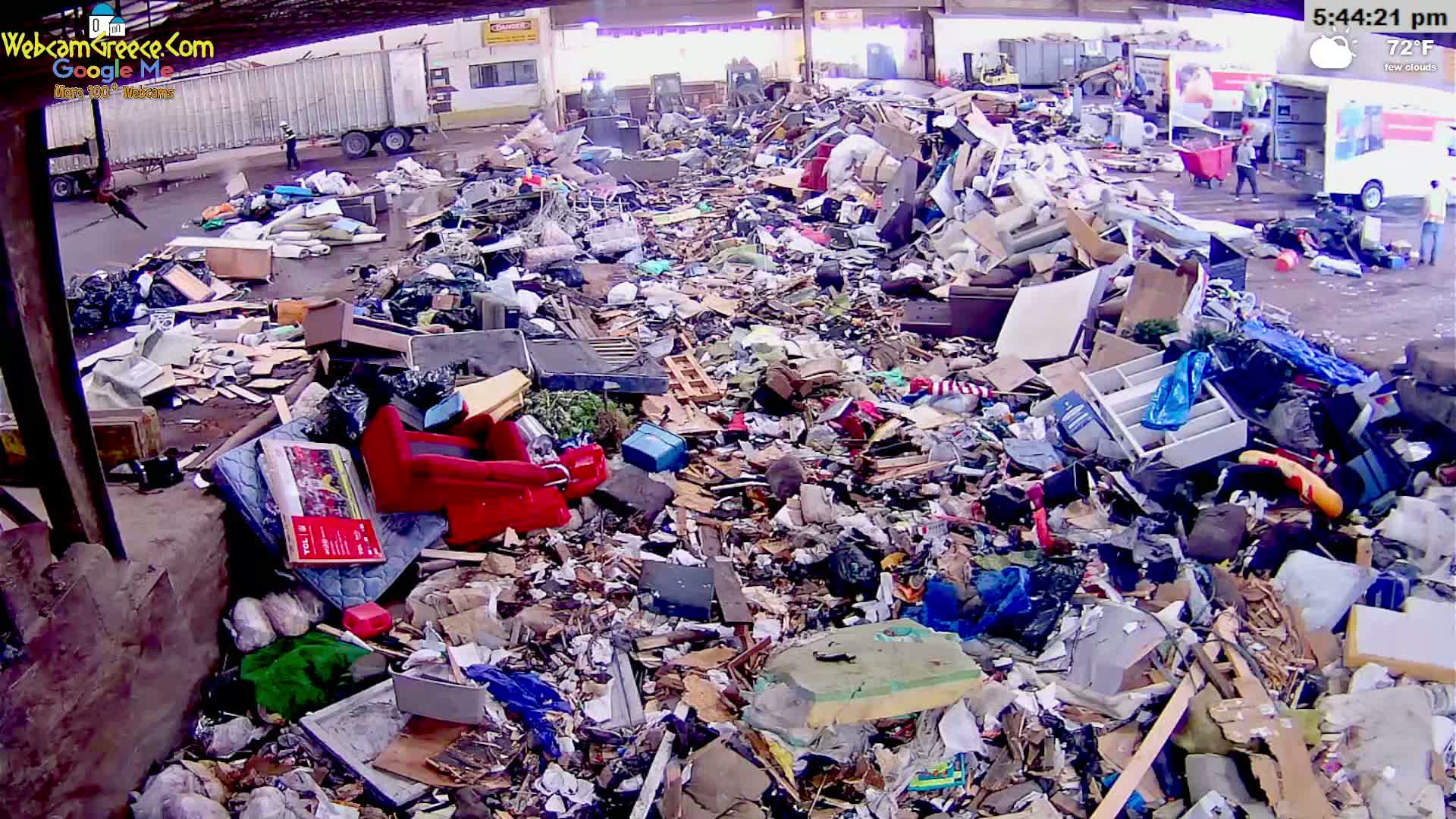 A large pile of discarded furniture, appliances, and other debris sits in an outdoor area under an overcast sky.