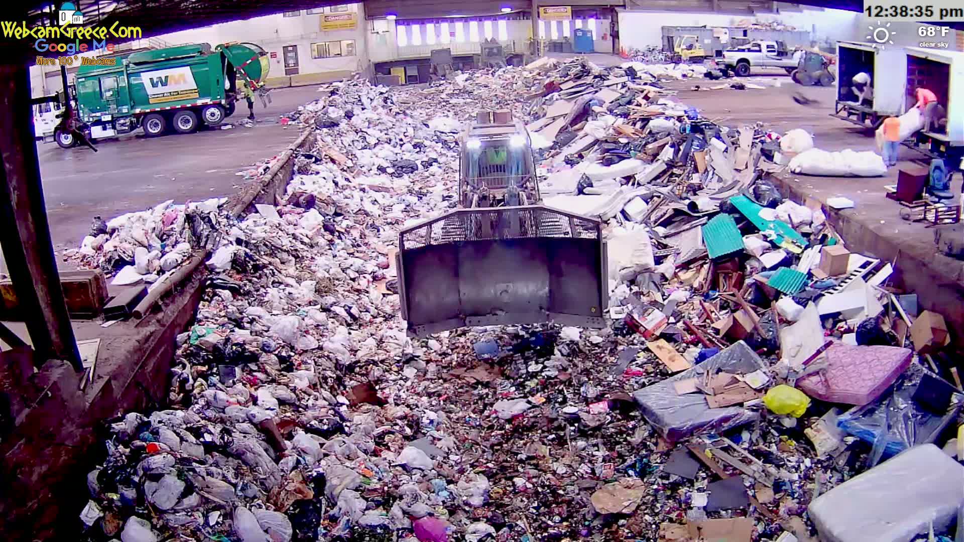 A bulldozer pushes a large pile of trash in a waste processing facility under a clear sky.