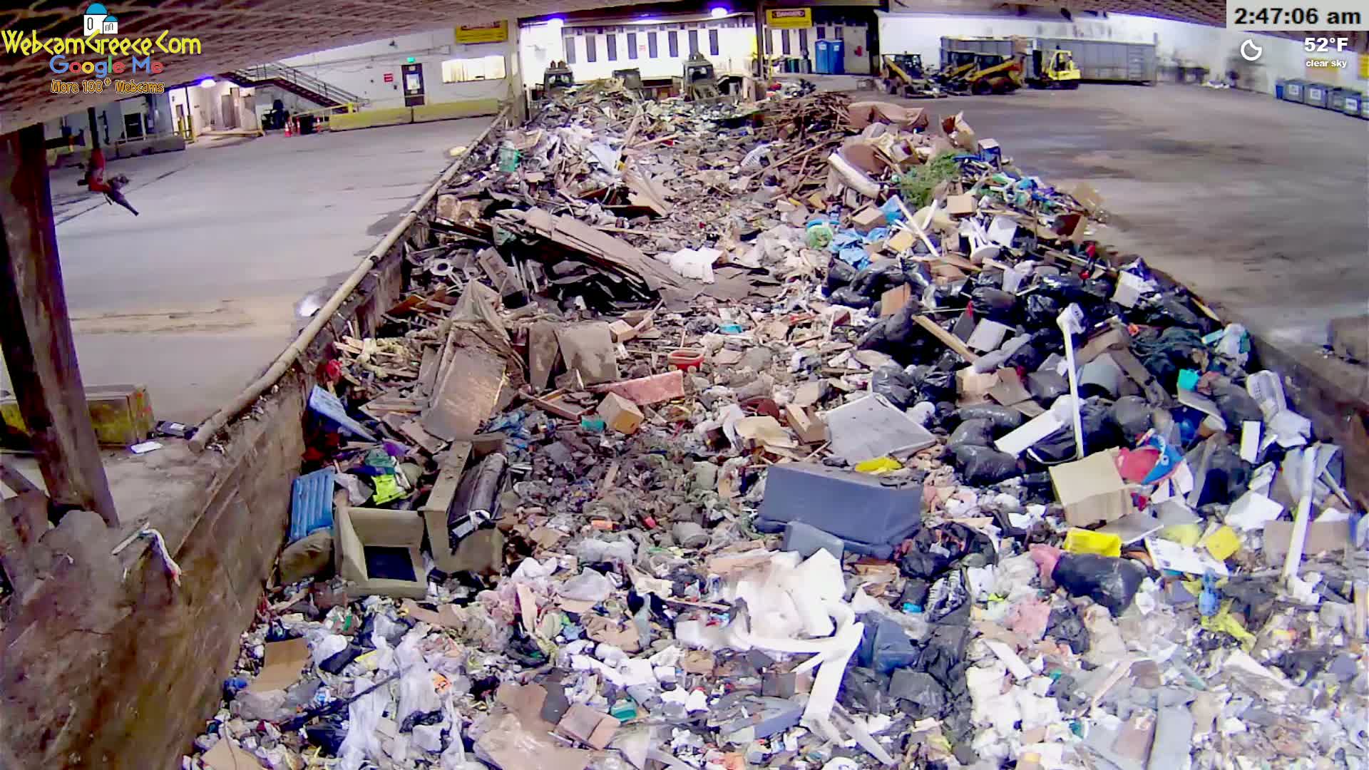 A large pile of mixed garbage and debris fills an indoor container under a clear sky.