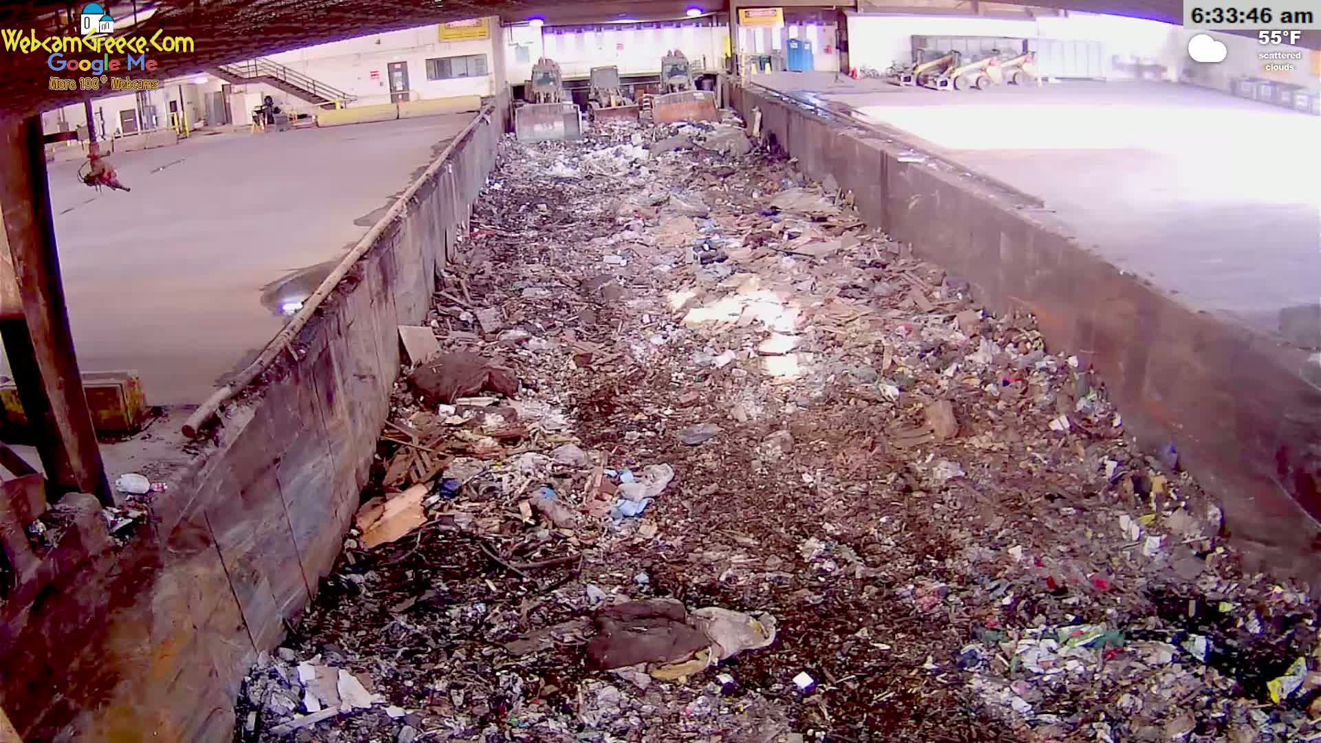 A large pile of refuse sits within a long, industrial trough under scattered clouds and a 55°F temperature.