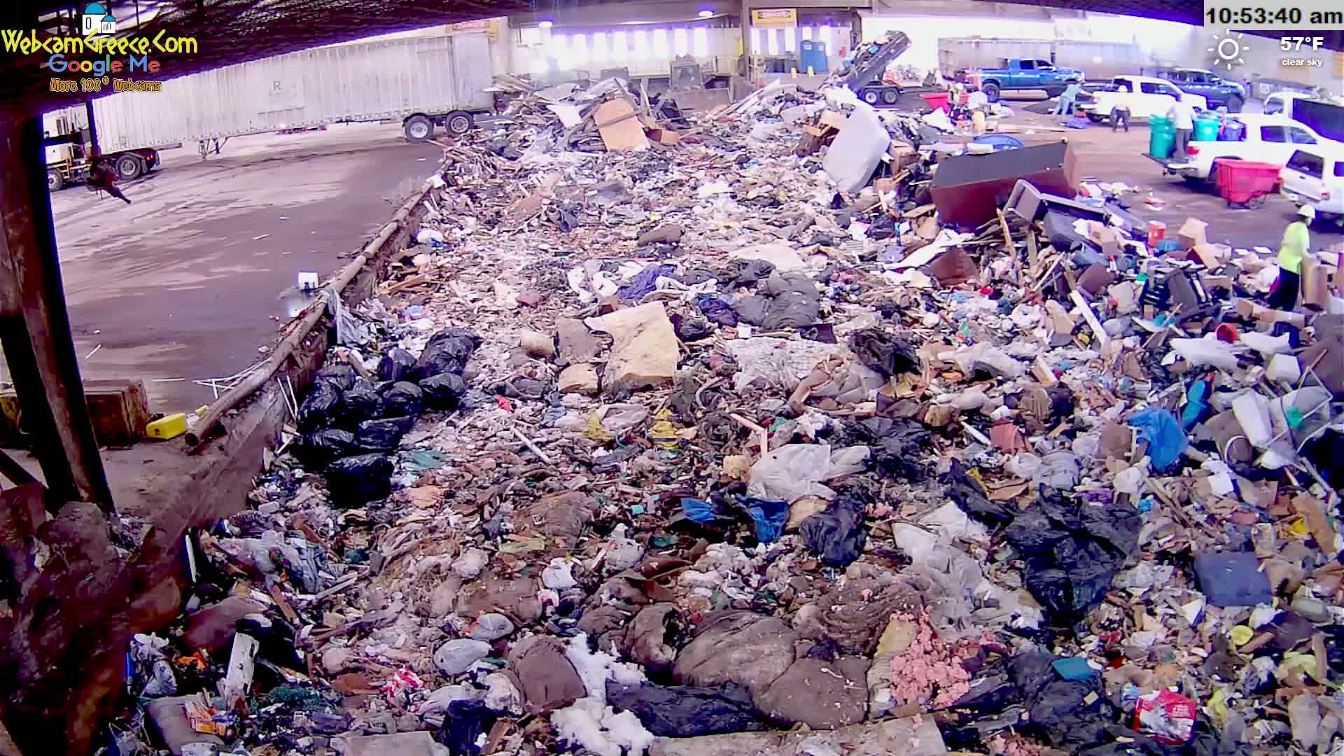 A large pile of refuse is seen outdoors on a clear, 57°F day, with several trucks and workers visible in the background.