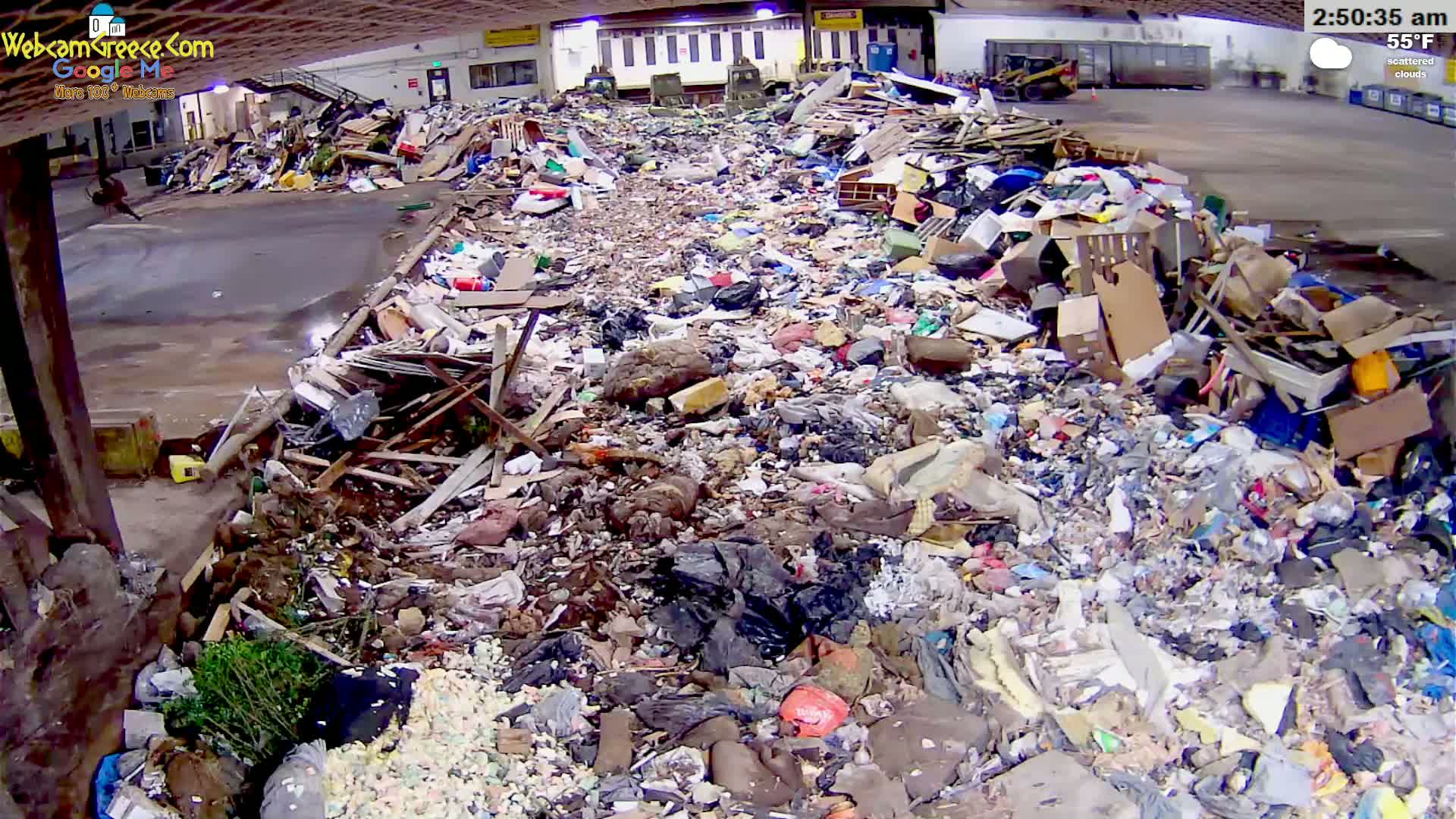 A large pile of mixed waste and debris sits under a covered structure in scattered cloud conditions.