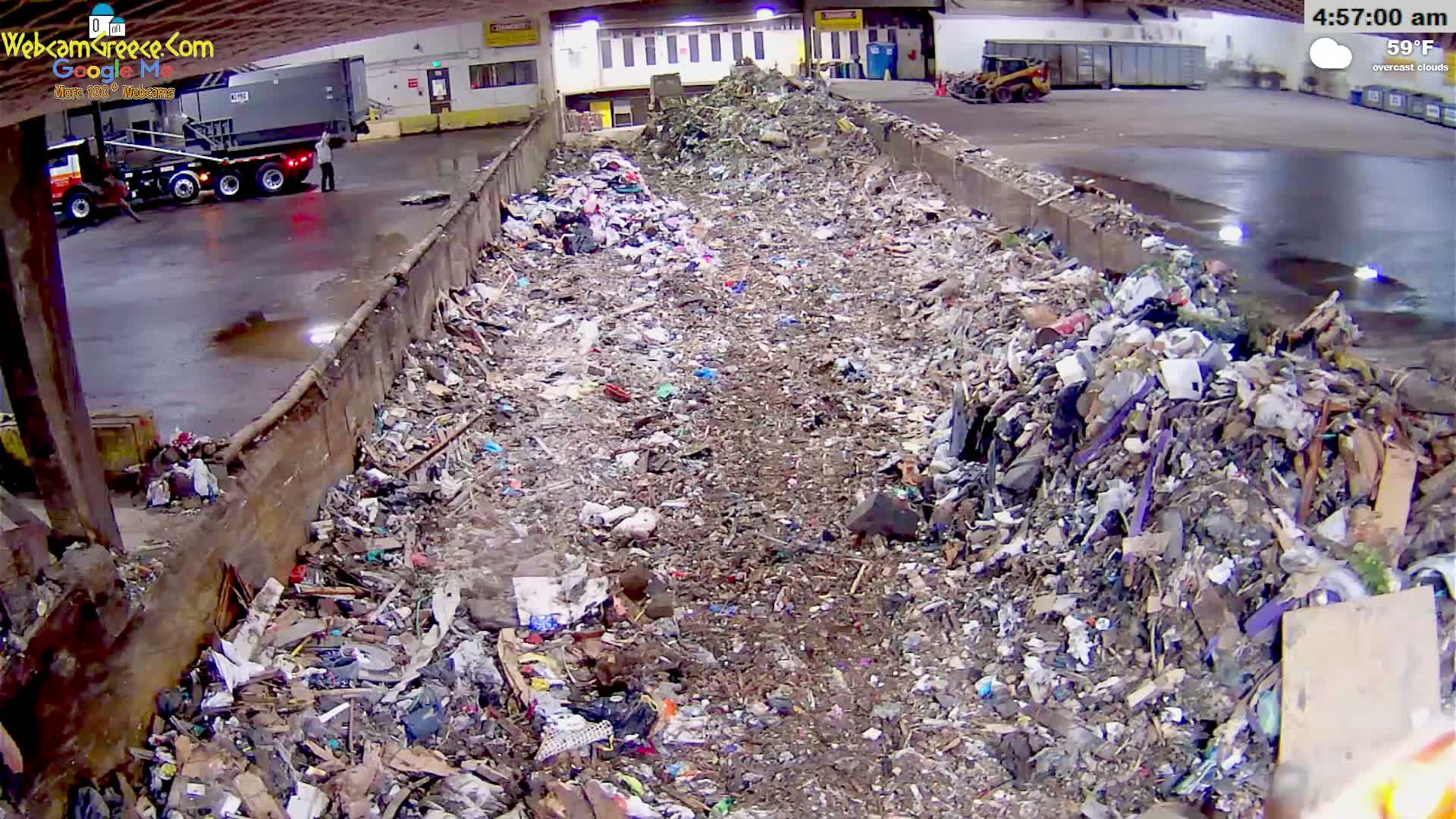 A large pile of trash sits in an indoor waste facility under overcast skies.