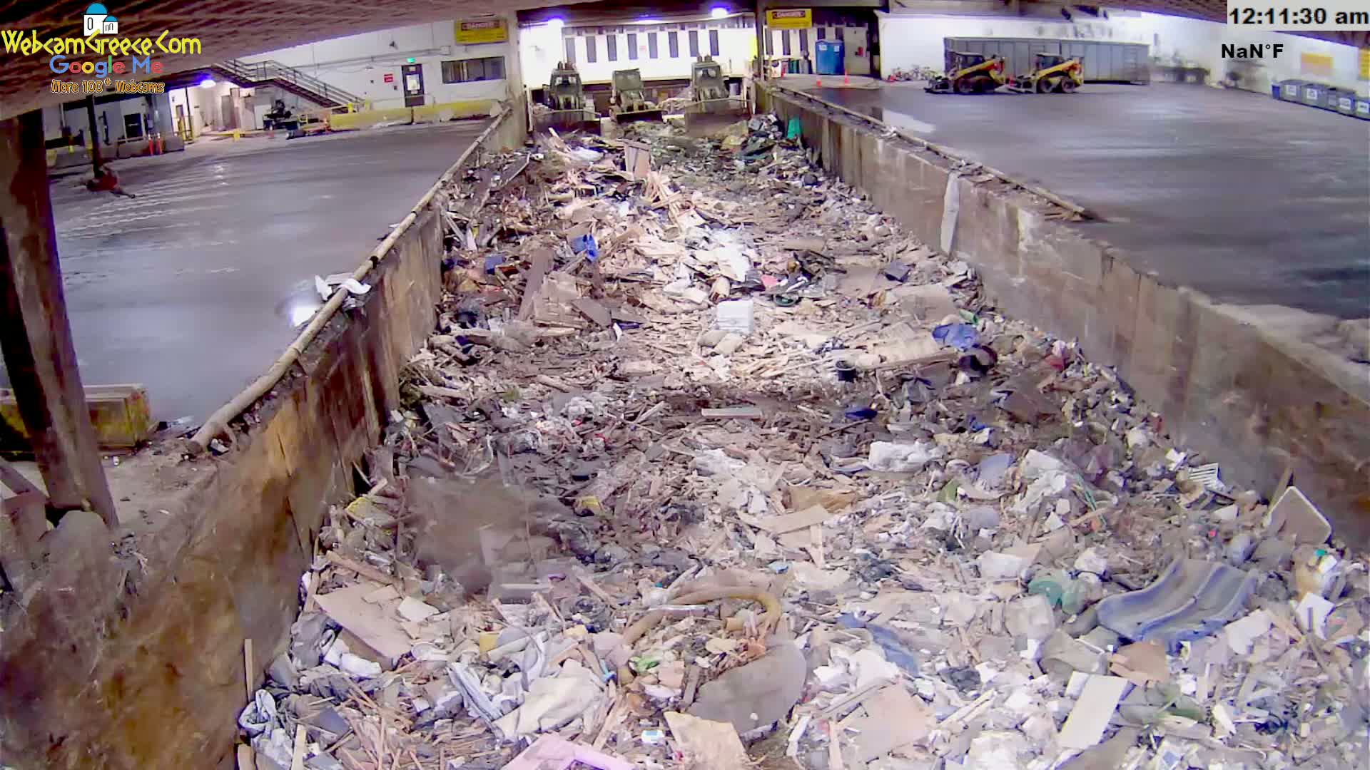 A large indoor waste disposal area contains a massive pile of mixed refuse, with two pieces of heavy machinery visible in the background.