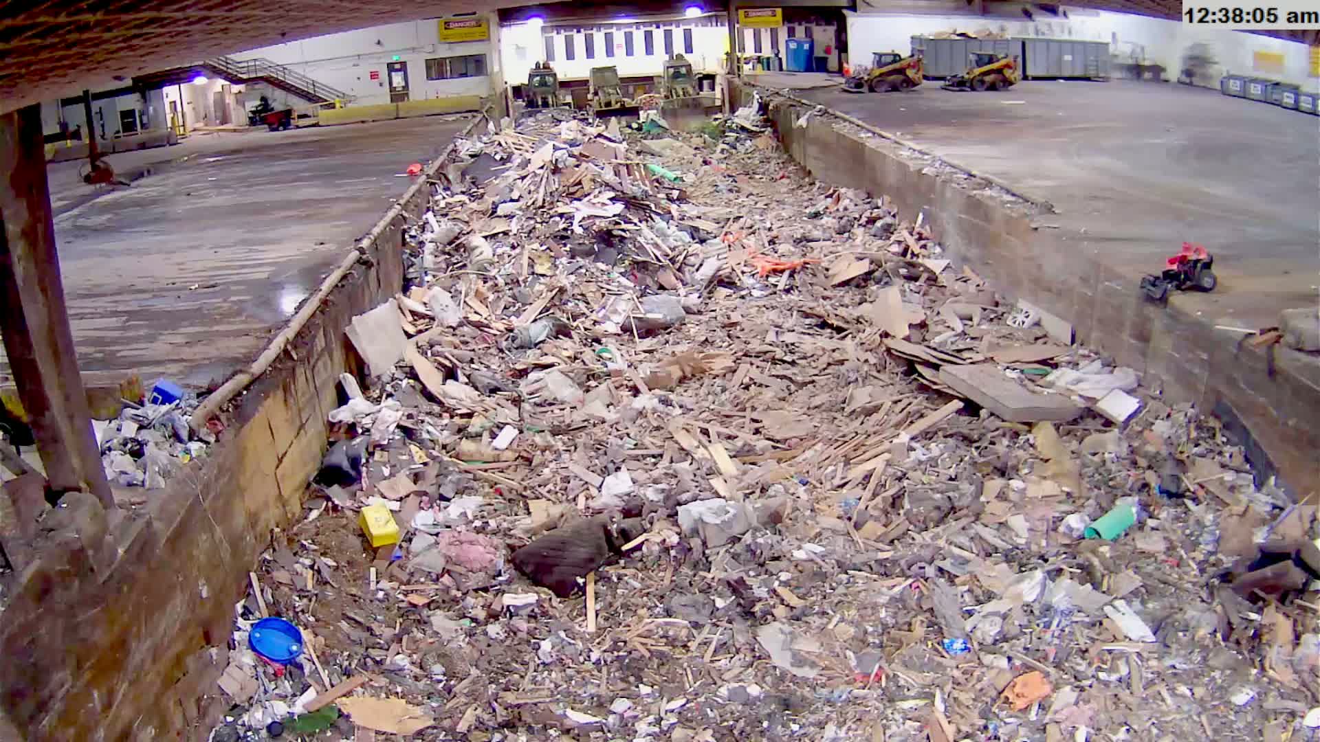 A large indoor bin is overflowing with a mixture of wood, debris, and other refuse.