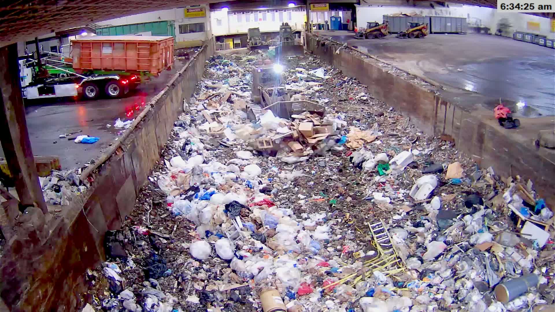A large indoor bin is overflowing with a mixture of wood, debris, and other refuse.