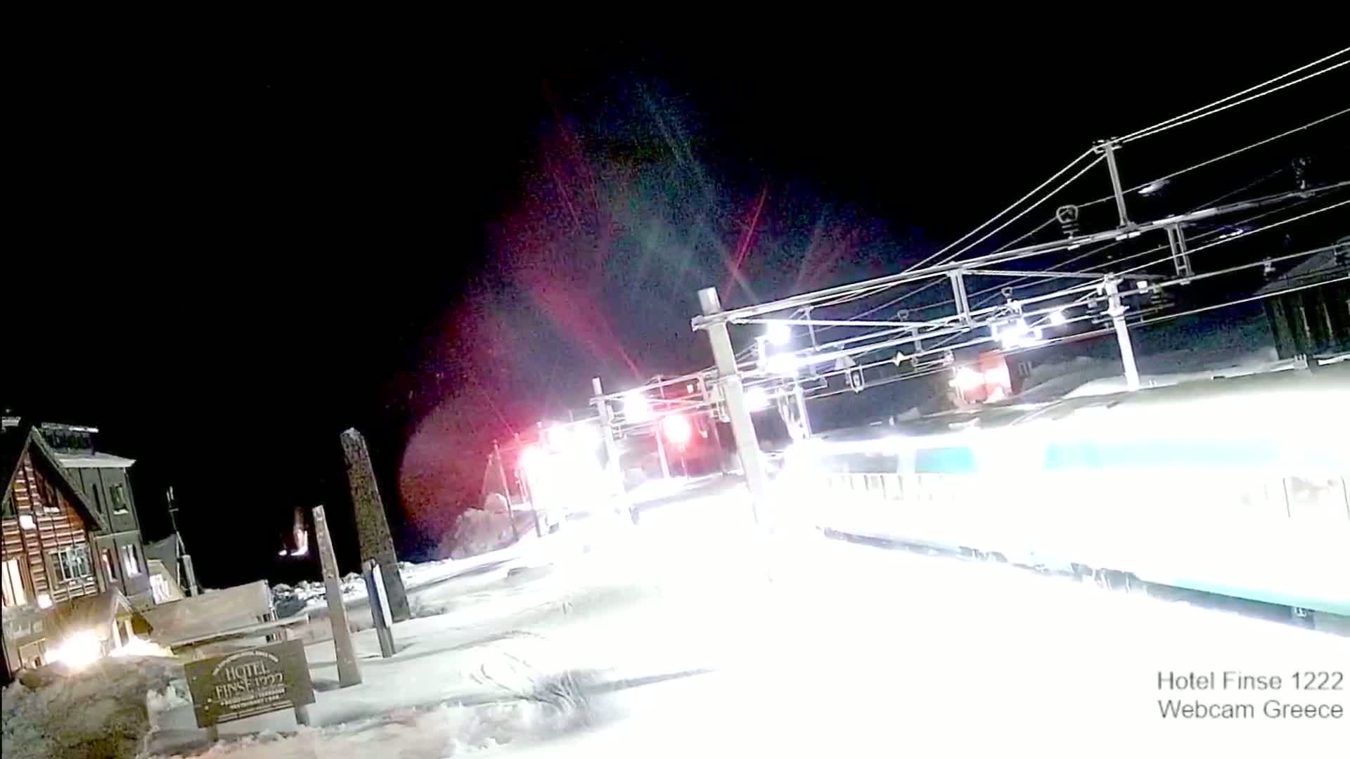 A long train passes a snow-covered train station at night.