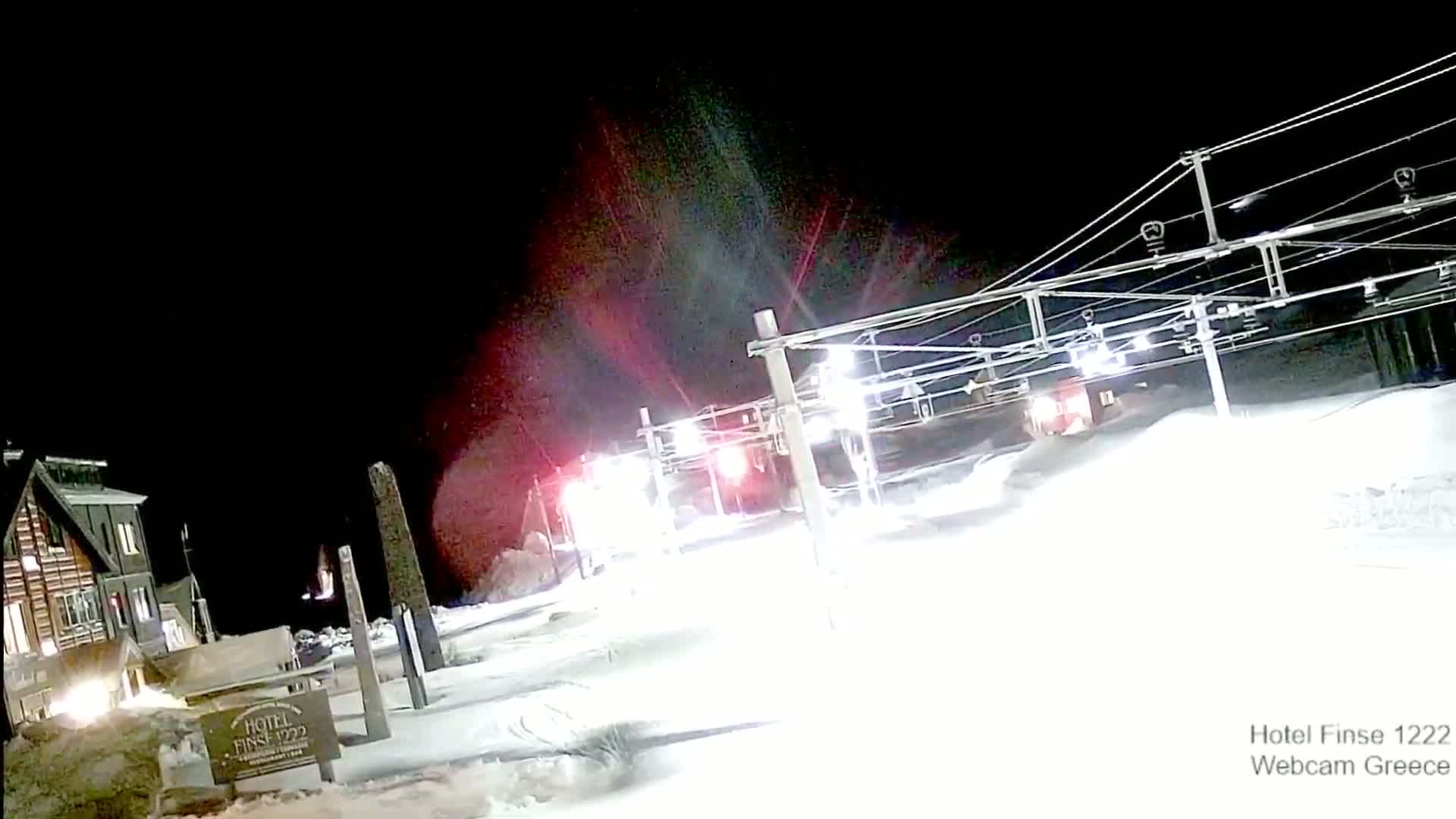 A nighttime view of a snow-covered area with a ski lift and a building illuminated, under a dark sky.