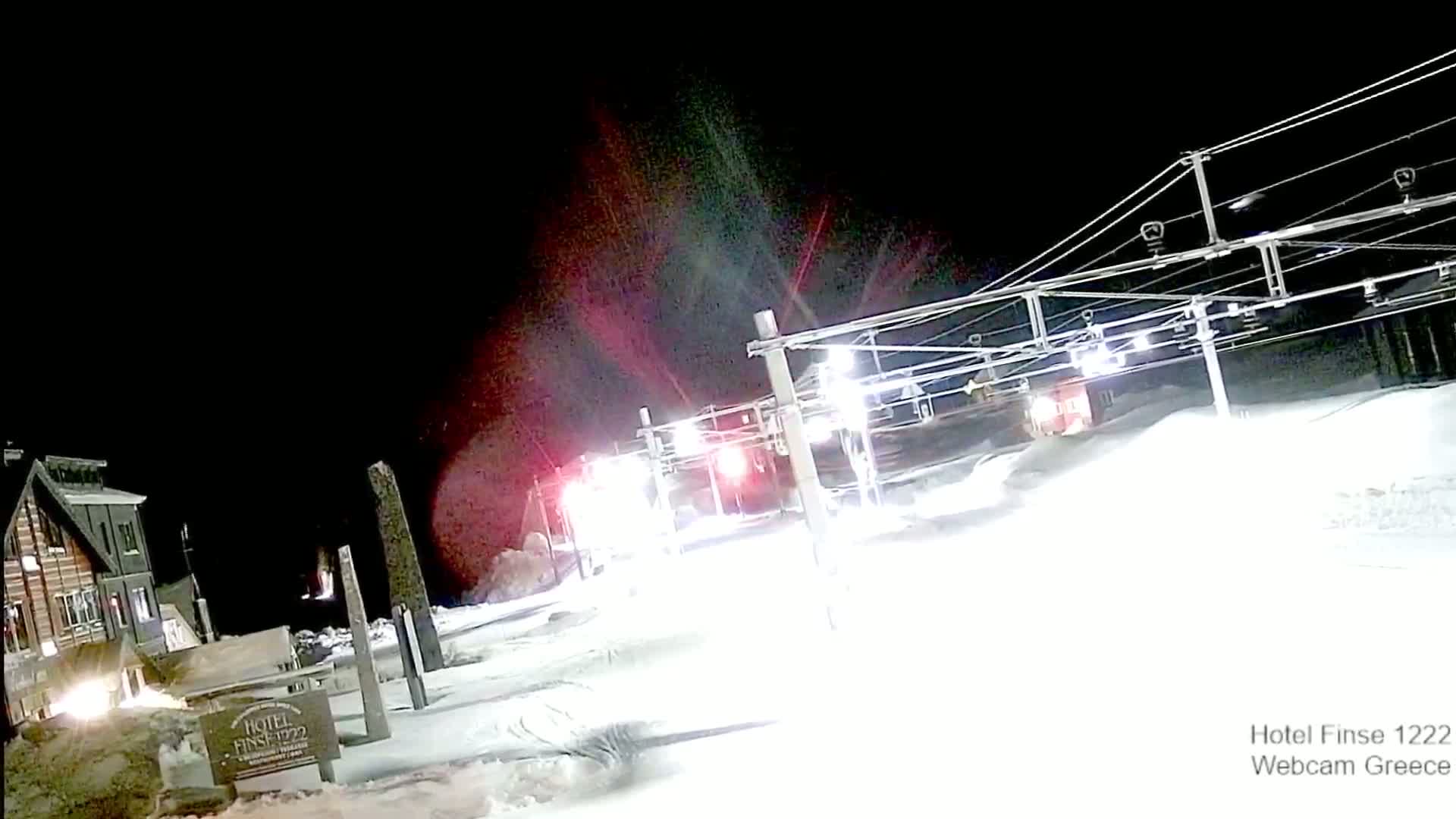 A nighttime view of a snow-covered ski lift and a building under a dark sky.