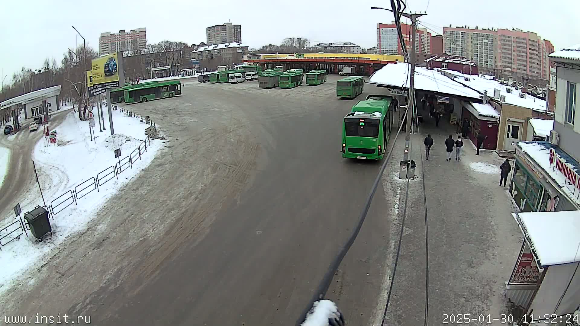 A bus station with numerous green buses parked in a snowy lot on an overcast day.