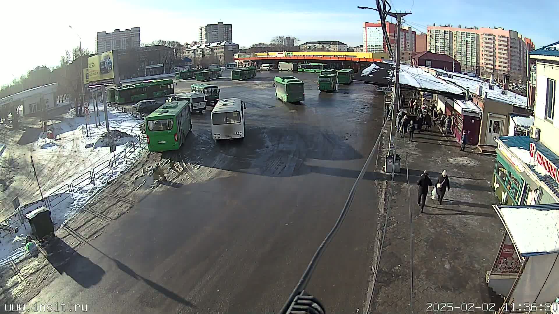 A bus depot with numerous buses parked in a large, wet, partly snow-covered lot on a sunny day.
