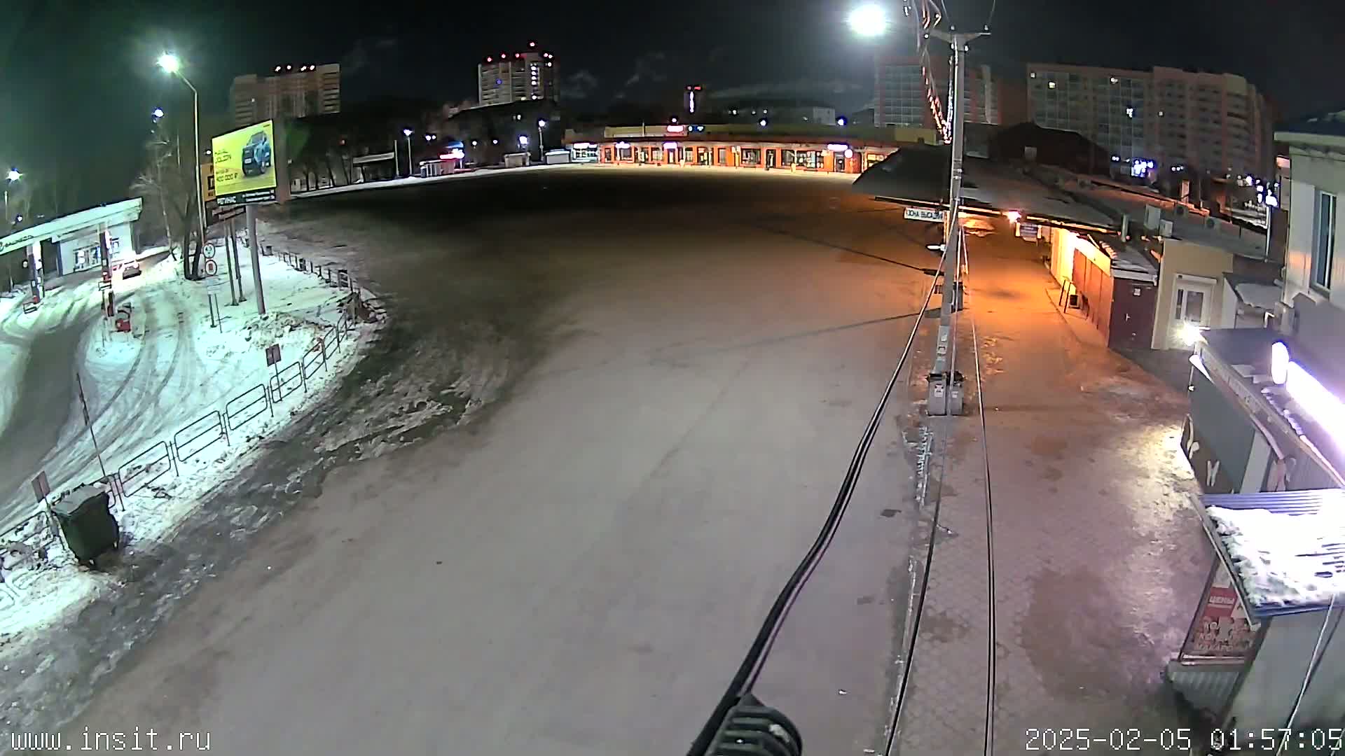 A nighttime, snow-dusted parking lot and street scene is visible, with multi-story buildings in the background under partly cloudy skies.