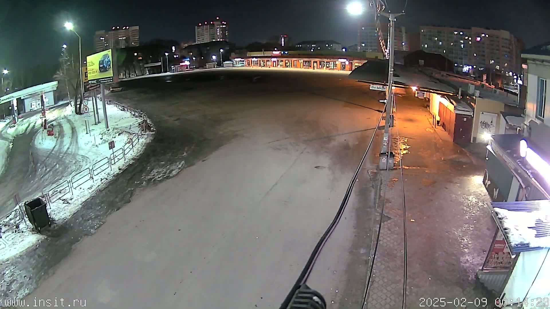 A nighttime, snow-dusted parking lot and roadway are visible, with buildings and streetlights in the background.