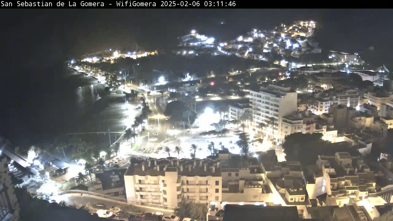 A nighttime aerial view of a coastal town with illuminated buildings and streets, beside a dark ocean.