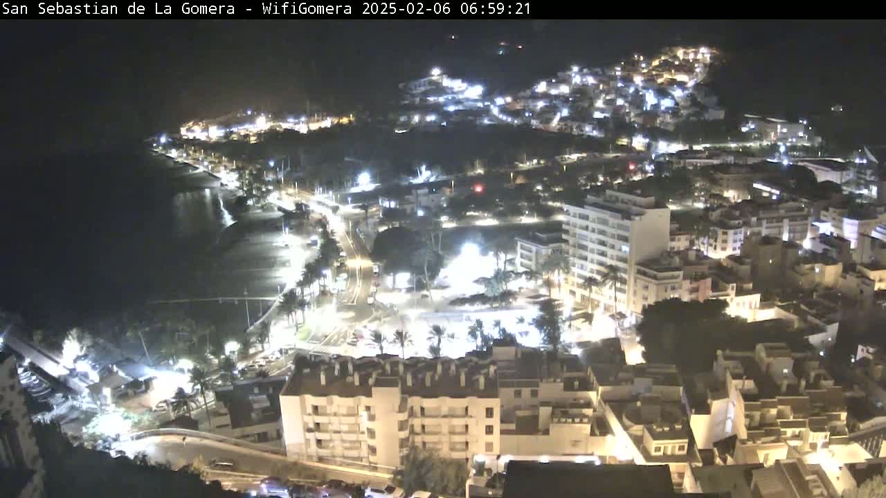 A nighttime aerial view of a coastal town, showing brightly lit buildings, streets, and a dark beach.