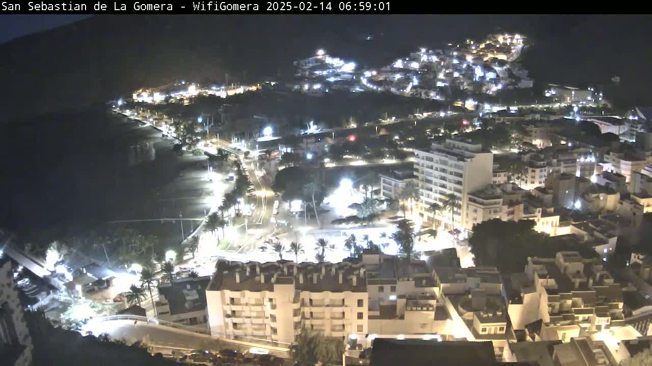A nighttime aerial view of a coastal town, showing illuminated buildings, streets, and a dark beach.