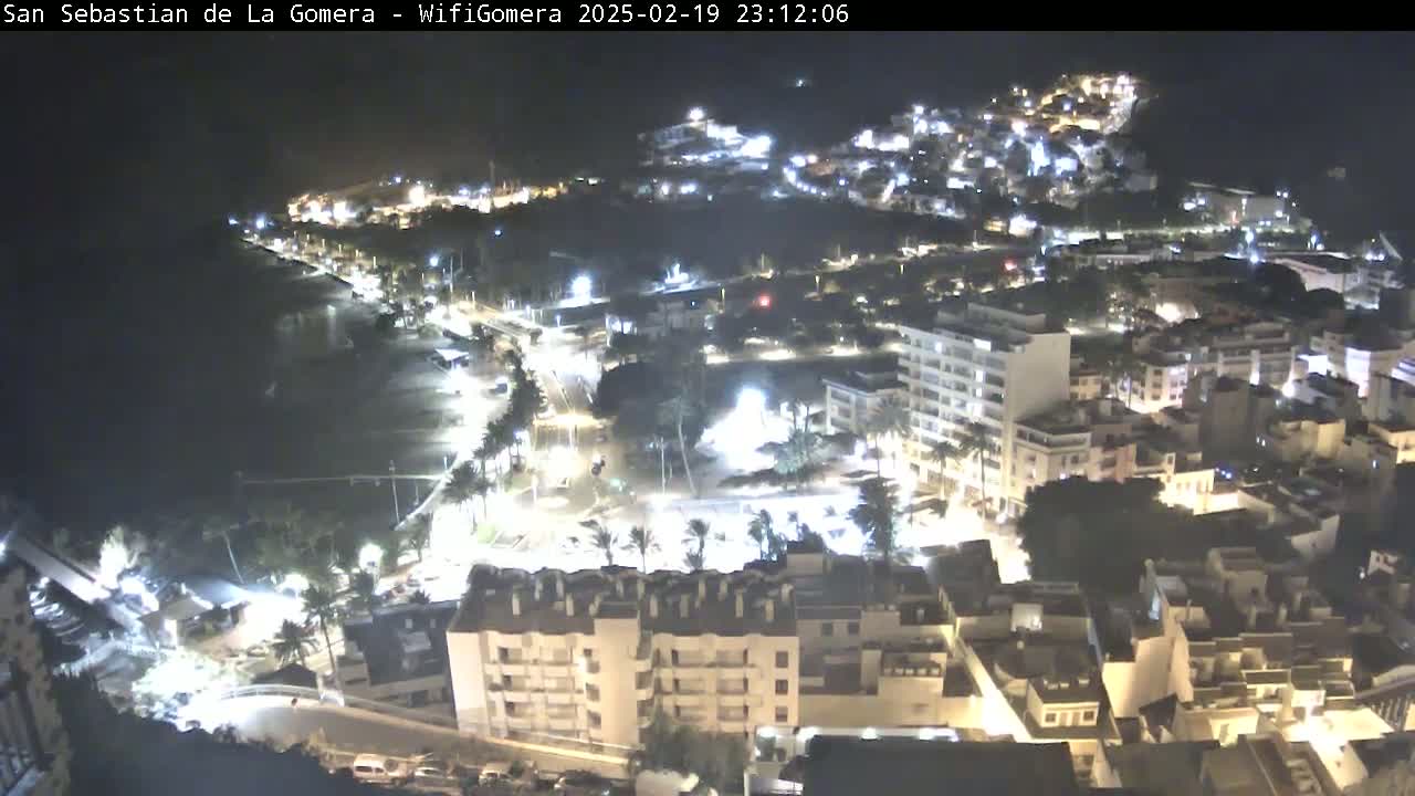 A nighttime aerial view of a coastal town, showing brightly lit buildings, streets, and a dark beach.