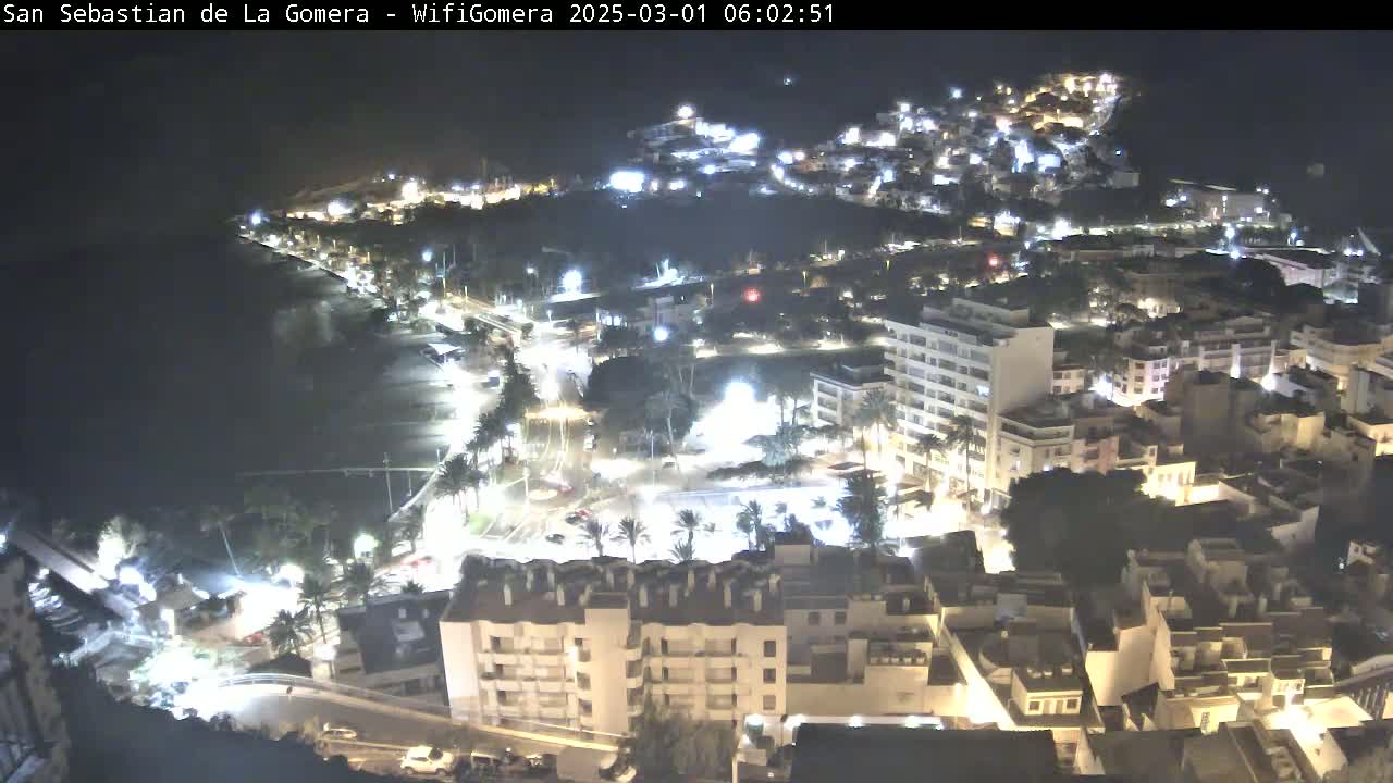 A nighttime aerial view of a coastal town, illuminated by streetlights, with a dark ocean in the background.