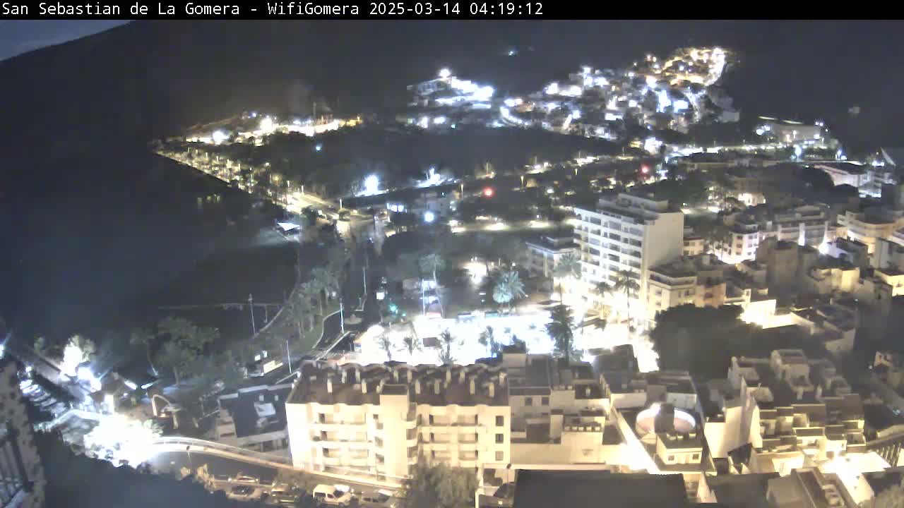 A nighttime aerial view of a coastal town, showing buildings illuminated against a dark ocean.