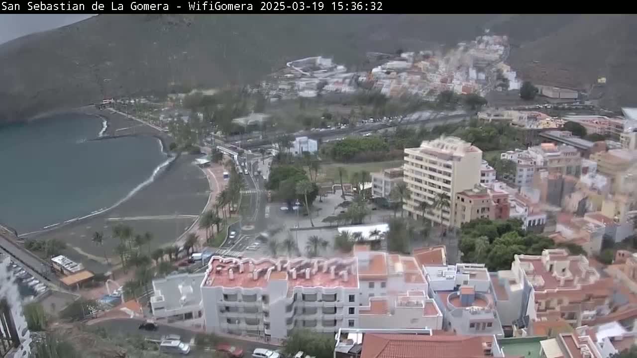 An overcast coastal town with dark-colored sand beach and buildings, viewed from a high vantage point.