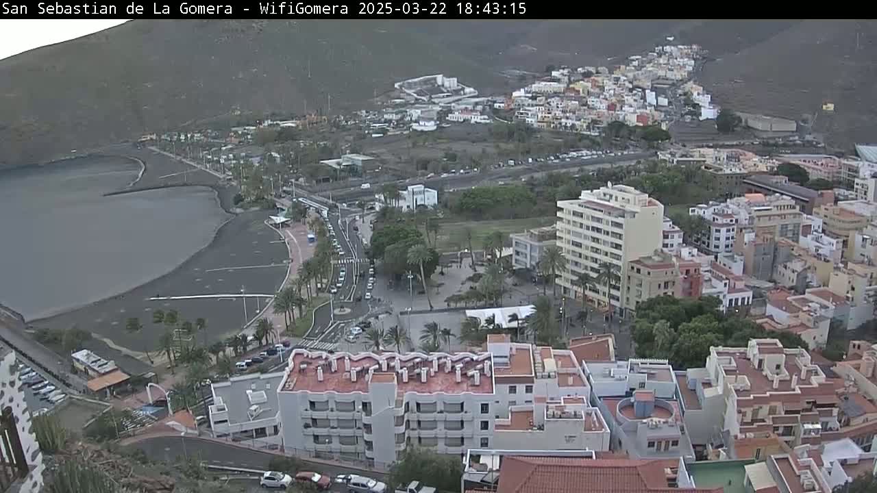 An overcast coastal town with a dark-sand beach and numerous buildings, seen from a high vantage point.