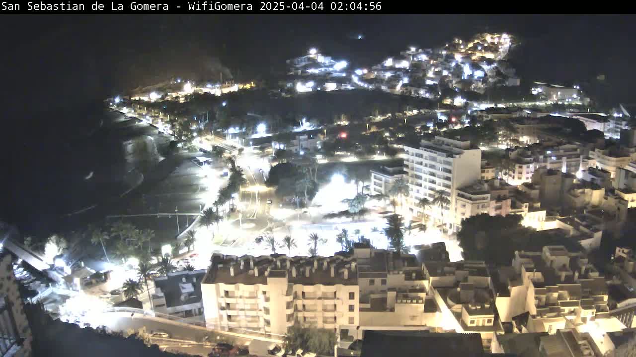 A nighttime, aerial view of a coastal town with a beach, buildings lit up, and dark ocean water.
