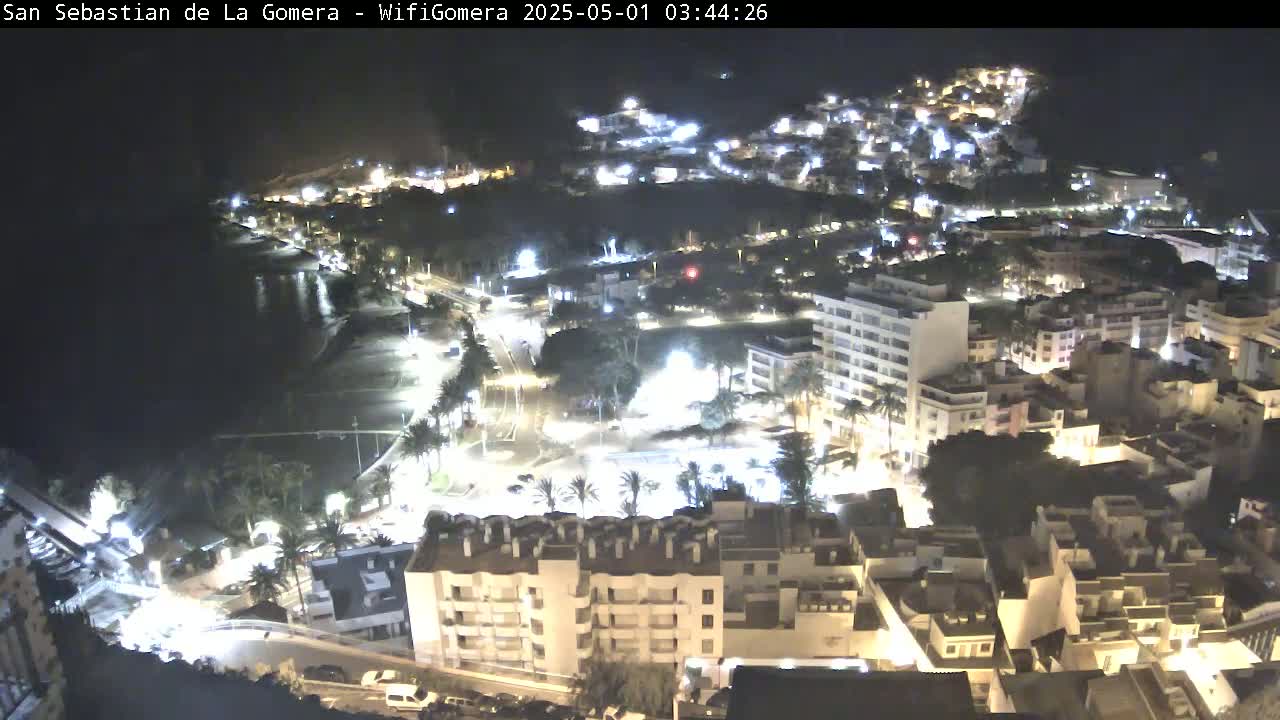 A nighttime aerial view of a coastal town, showing illuminated buildings, streets, and a dark ocean.
