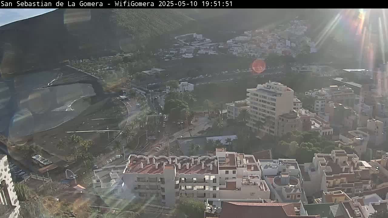 A hazy, sunny view overlooks a coastal town with buildings clustered near a dark-sand beach.