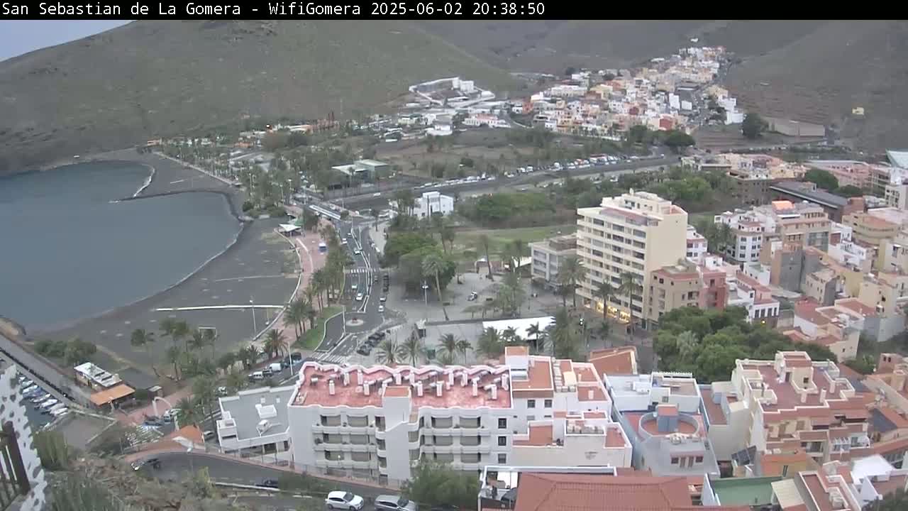A coastal town with dark-colored sand beaches and multistory buildings is seen under overcast skies.