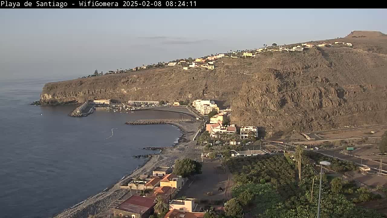 A coastal town nestled against a rocky hillside overlooking a calm bay under a clear sky.