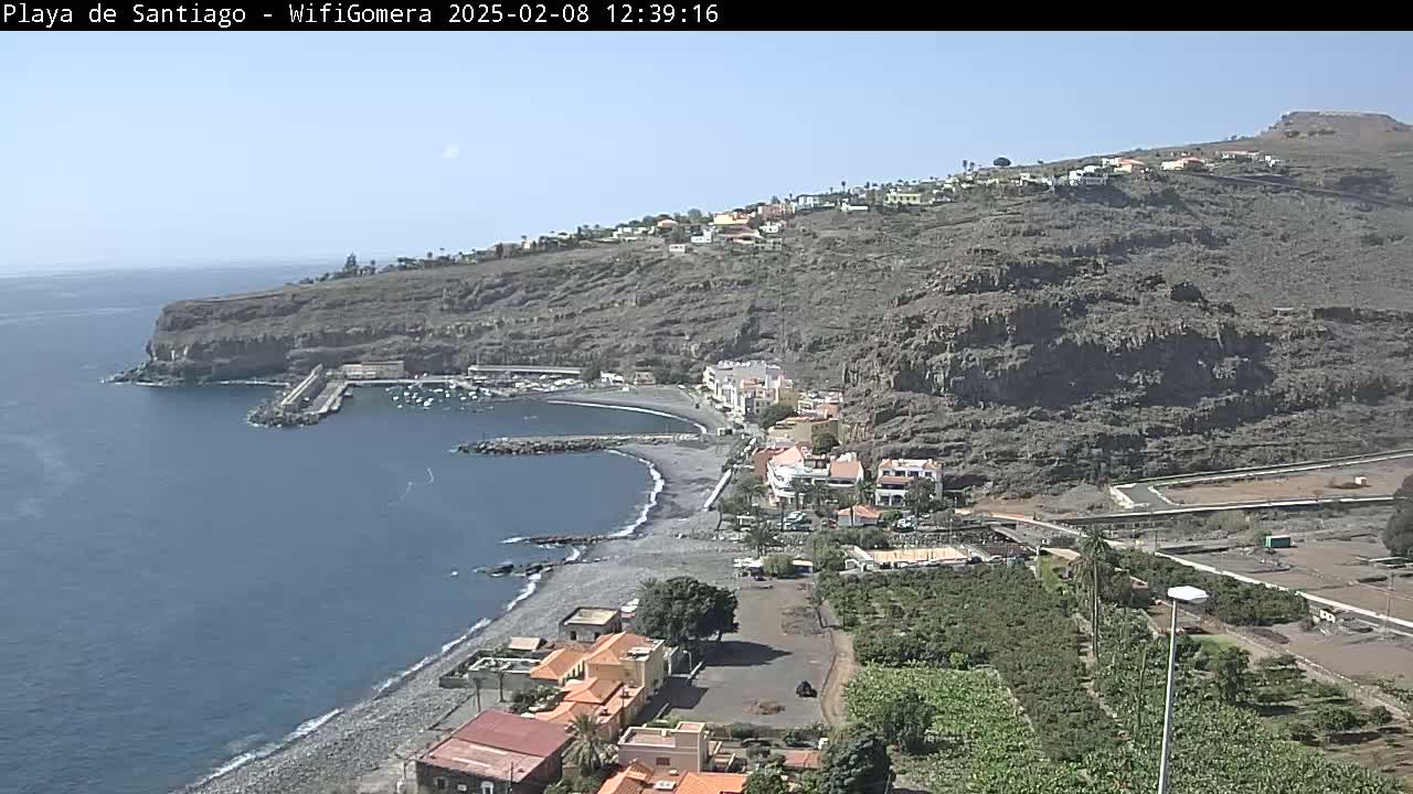 A coastal town nestled against a rocky hillside overlooks a calm bay on a sunny day.