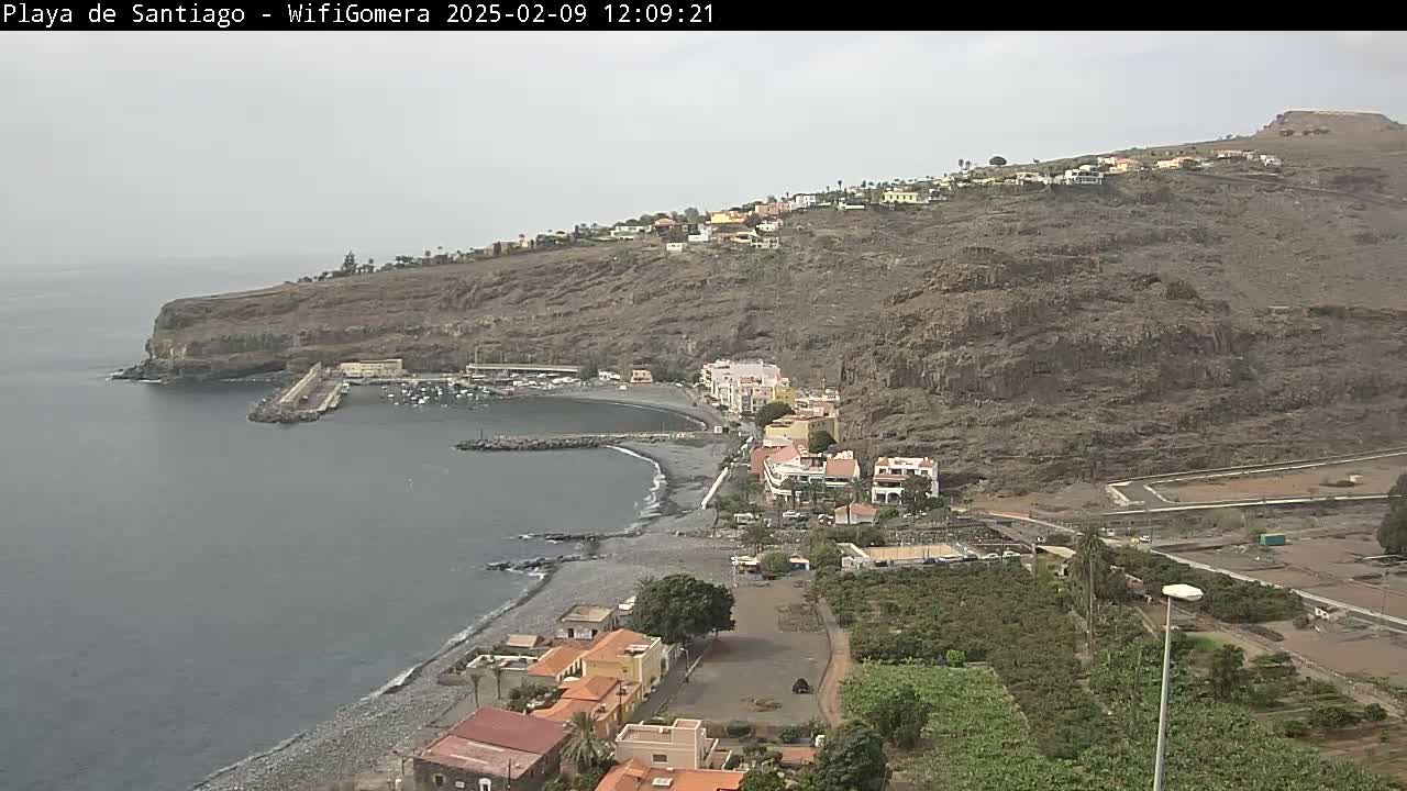 A coastal town nestled against a rocky hillside overlooks a calm bay on an overcast day.