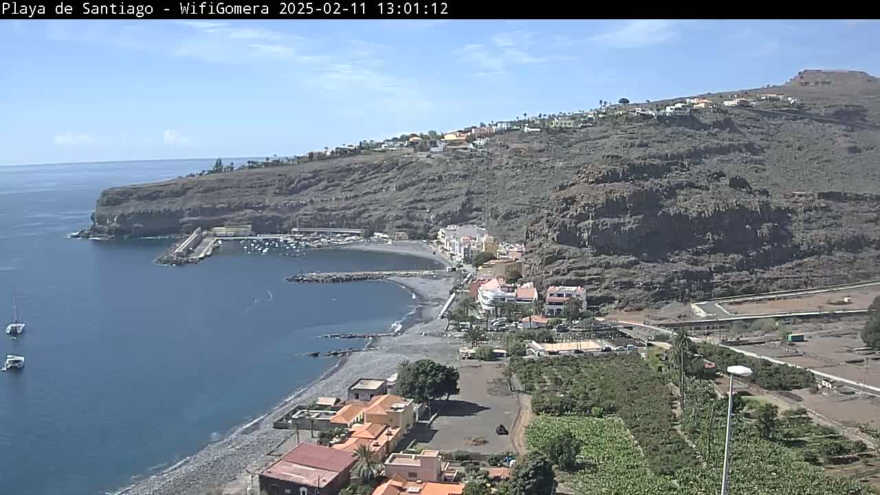 A coastal town nestled against a rocky hillside, with a small harbor and a dark-sand beach, under sunny skies.