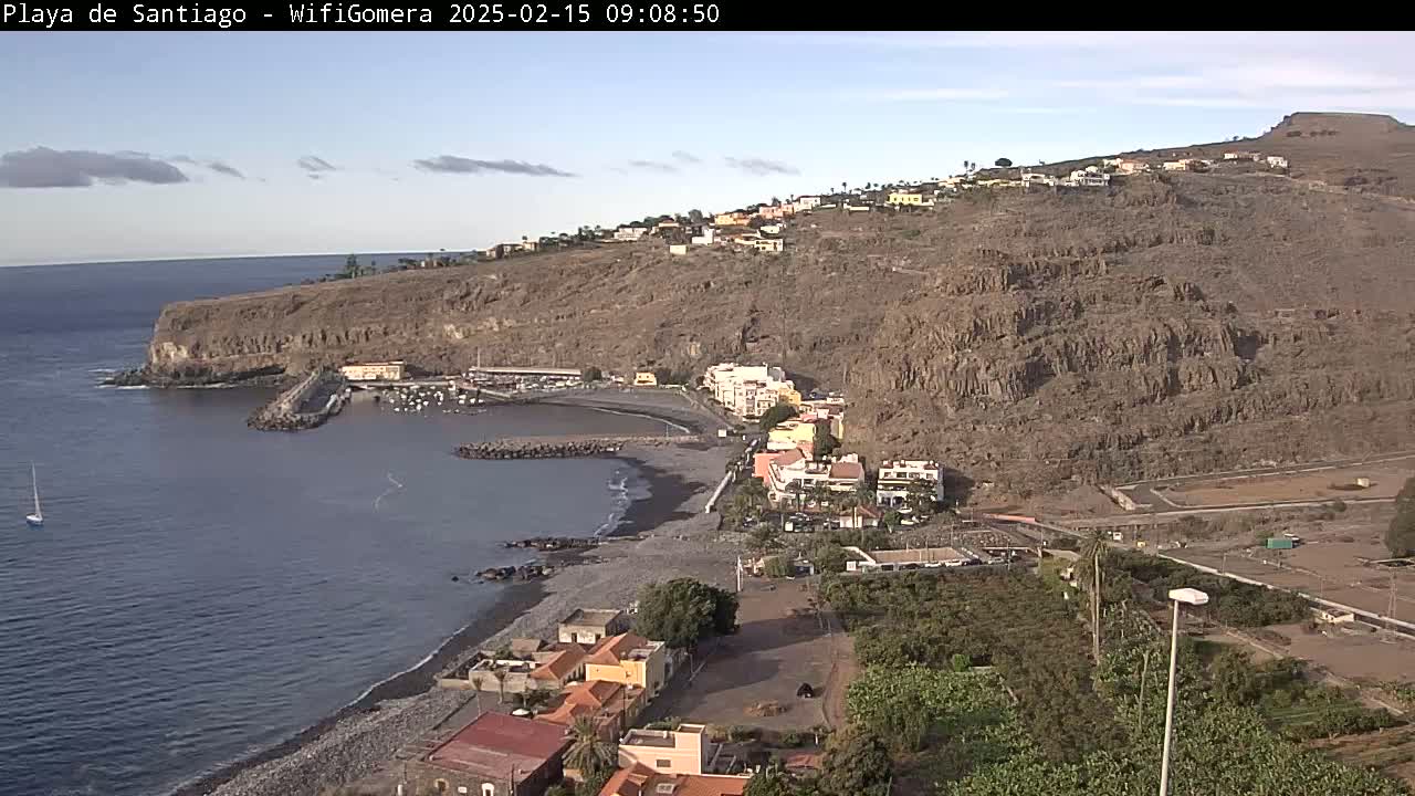 A coastal town with a small harbor nestled against a rocky, arid hillside under a mostly clear sky.