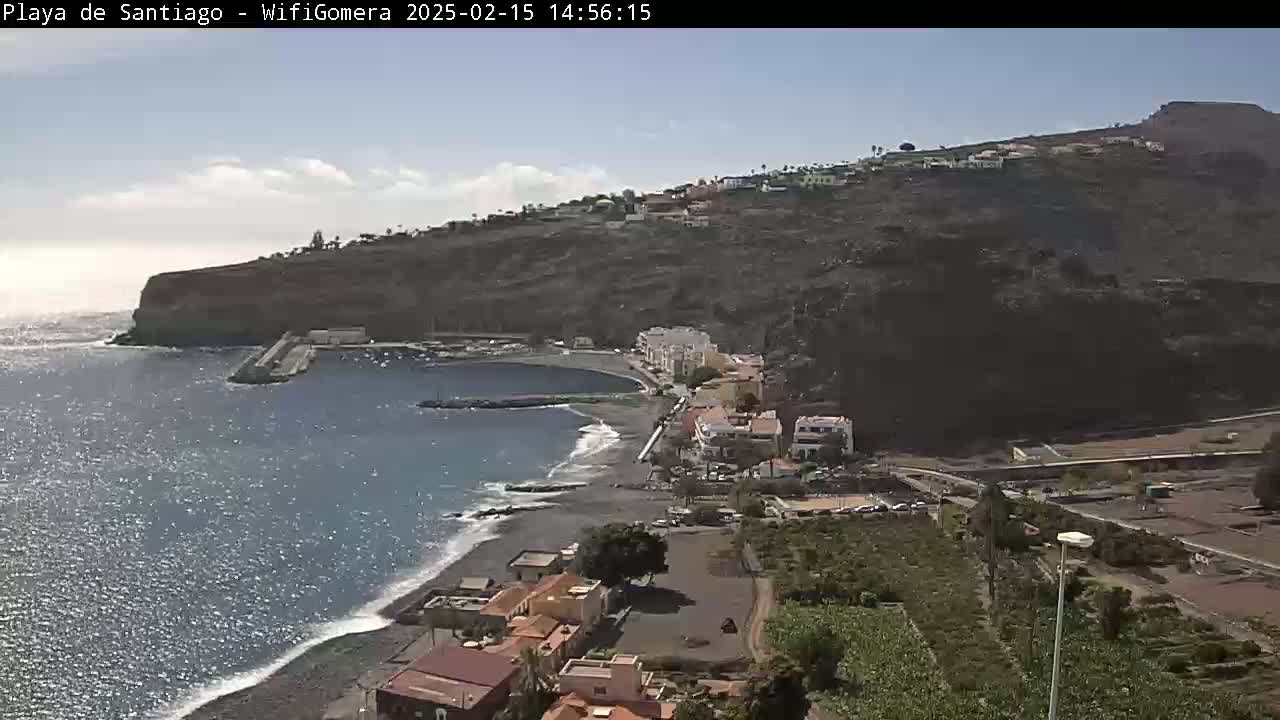 A coastal town nestled against a dark, rocky cliff overlooking a calm, blue ocean with a small beach.