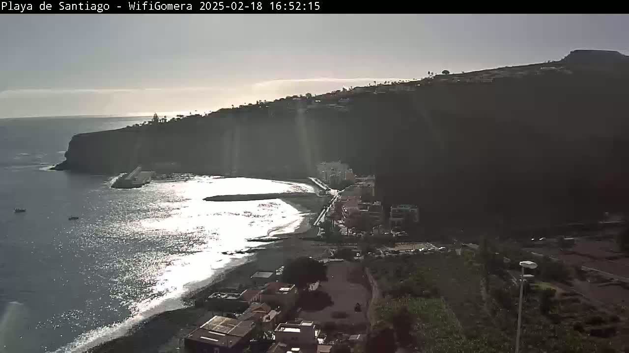A dark, rocky cliff overlooking a calm, sunlit ocean with a small town nestled at its base.