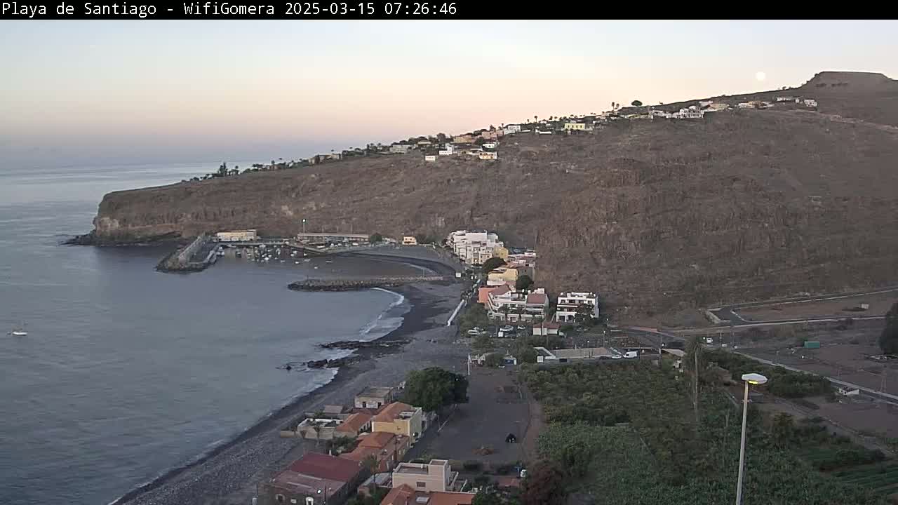 A coastal town nestled against a rocky hillside overlooks a calm ocean under a twilight sky.